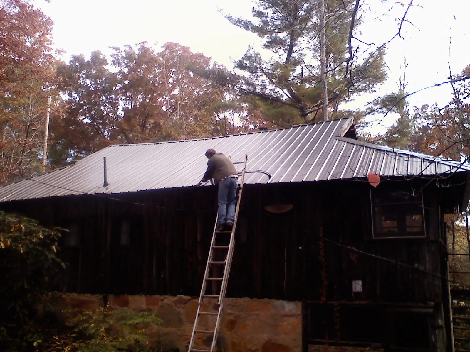 Roofer on a ladder working along the edge of a cabin metal roof in Saint Paul